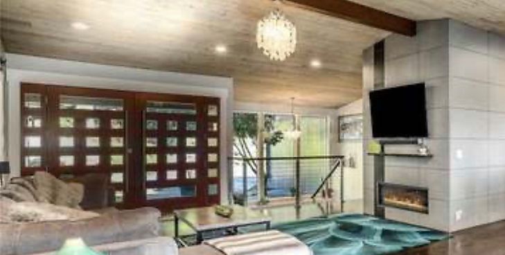 A modern living room features a wooden ceiling, a fireplace with a mounted television, and large paneled sliding doors.