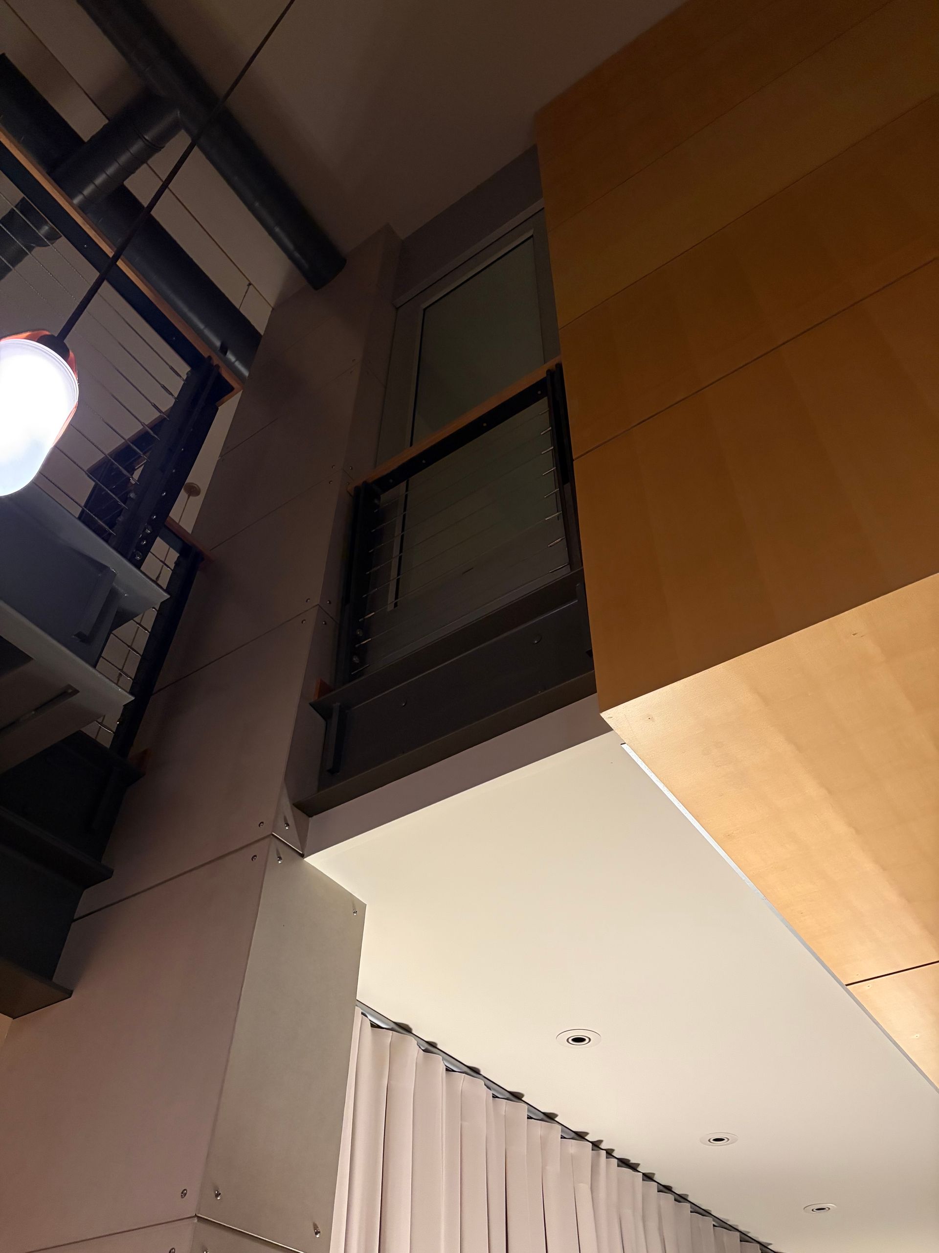 Low-angle view of a modern interior corner featuring a tall, wood-paneled column, a dark window frame, and white curtains.