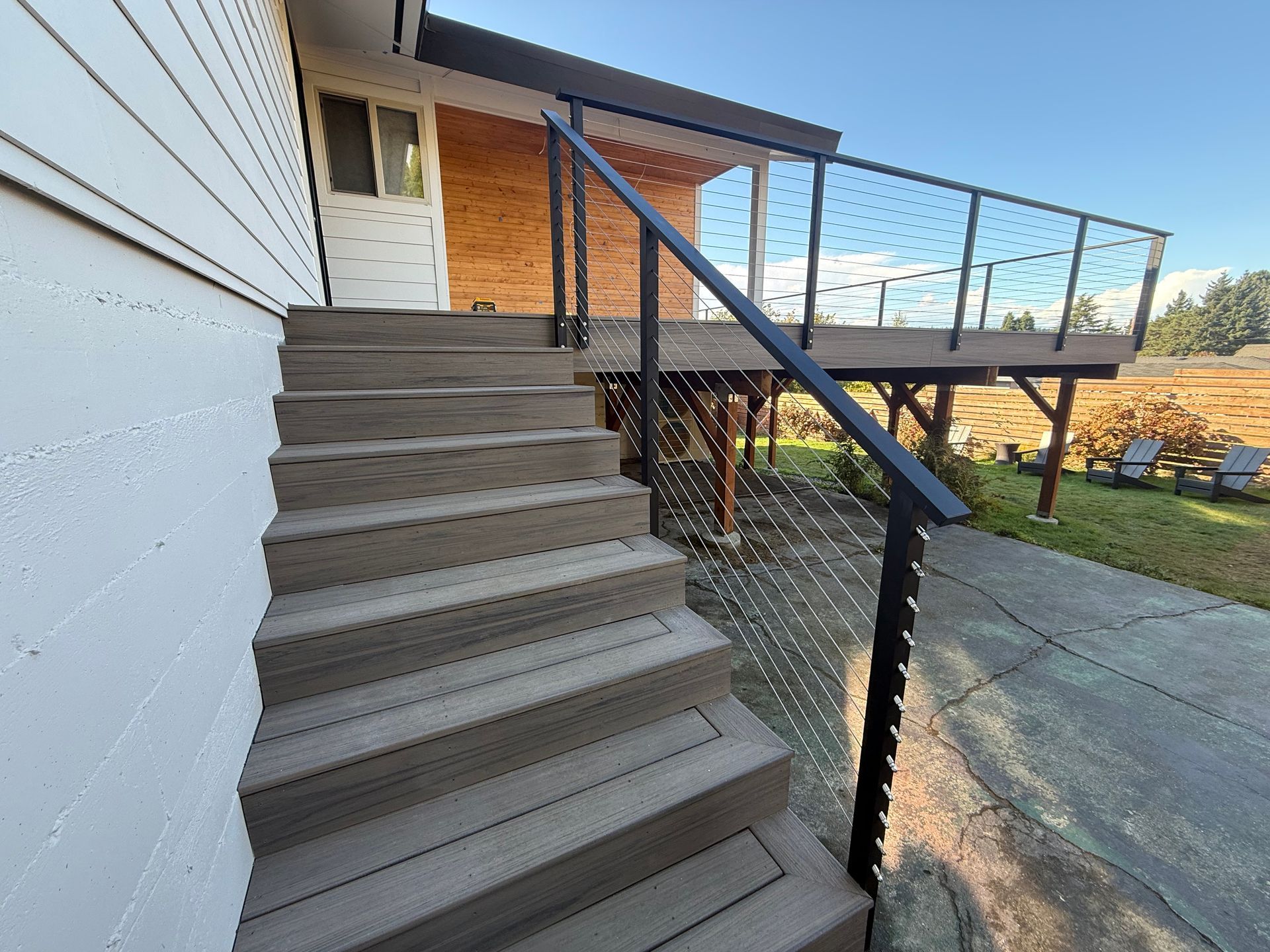Exterior view of gray composite stairs leading up to a wooden deck with a black metal railing and cable infill.