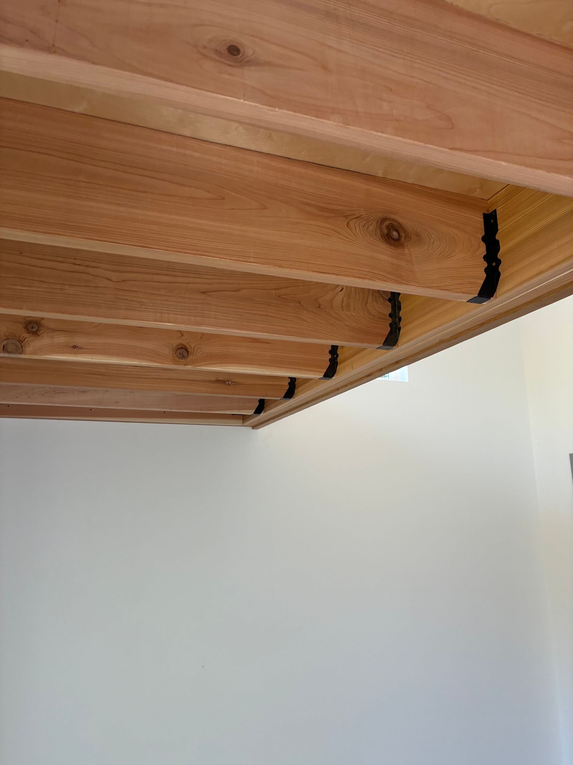 Exposed wooden ceiling beams with dark hardware brackets, set against a plain white wall.