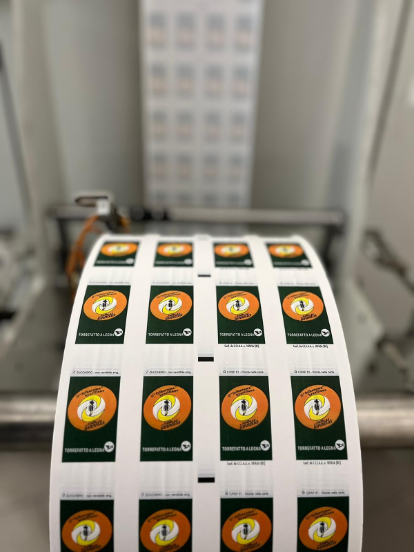 Un rotolo di etichette stampate con un disegno circolare arancione e verde. Il rotolo è in una macchina.