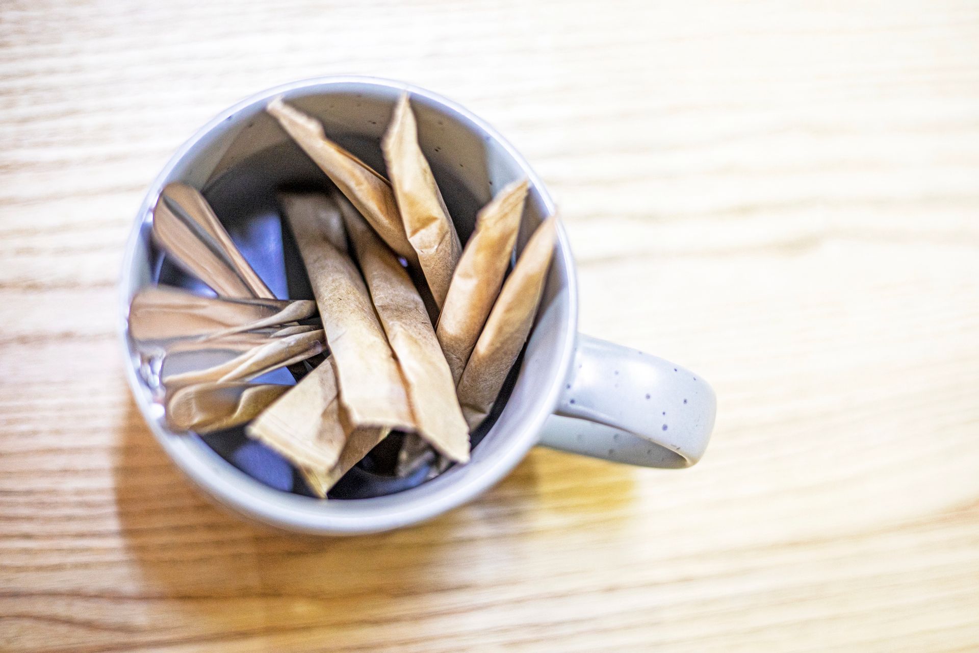 Una tazza di ceramica contenente diverse bustine di carta marrone chiaro piegate, posta su una superficie di legno.