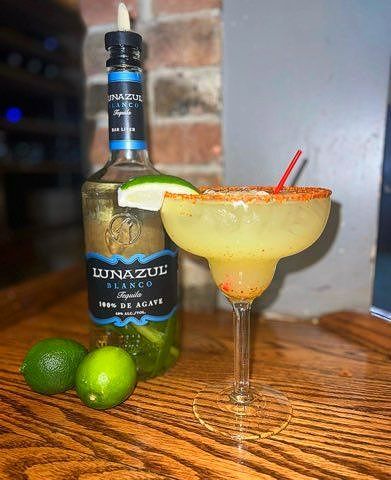 A margarita in a glass next to a bottle of tequila on a wooden table.