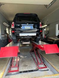 Black SUV on a red car lift inside a garage, viewed from the rear.