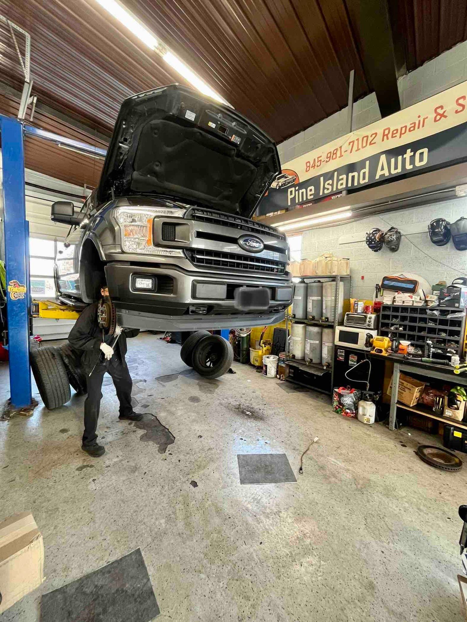 Mechanic working on a black truck lifted in an auto shop, Fire Island Auto sign above.