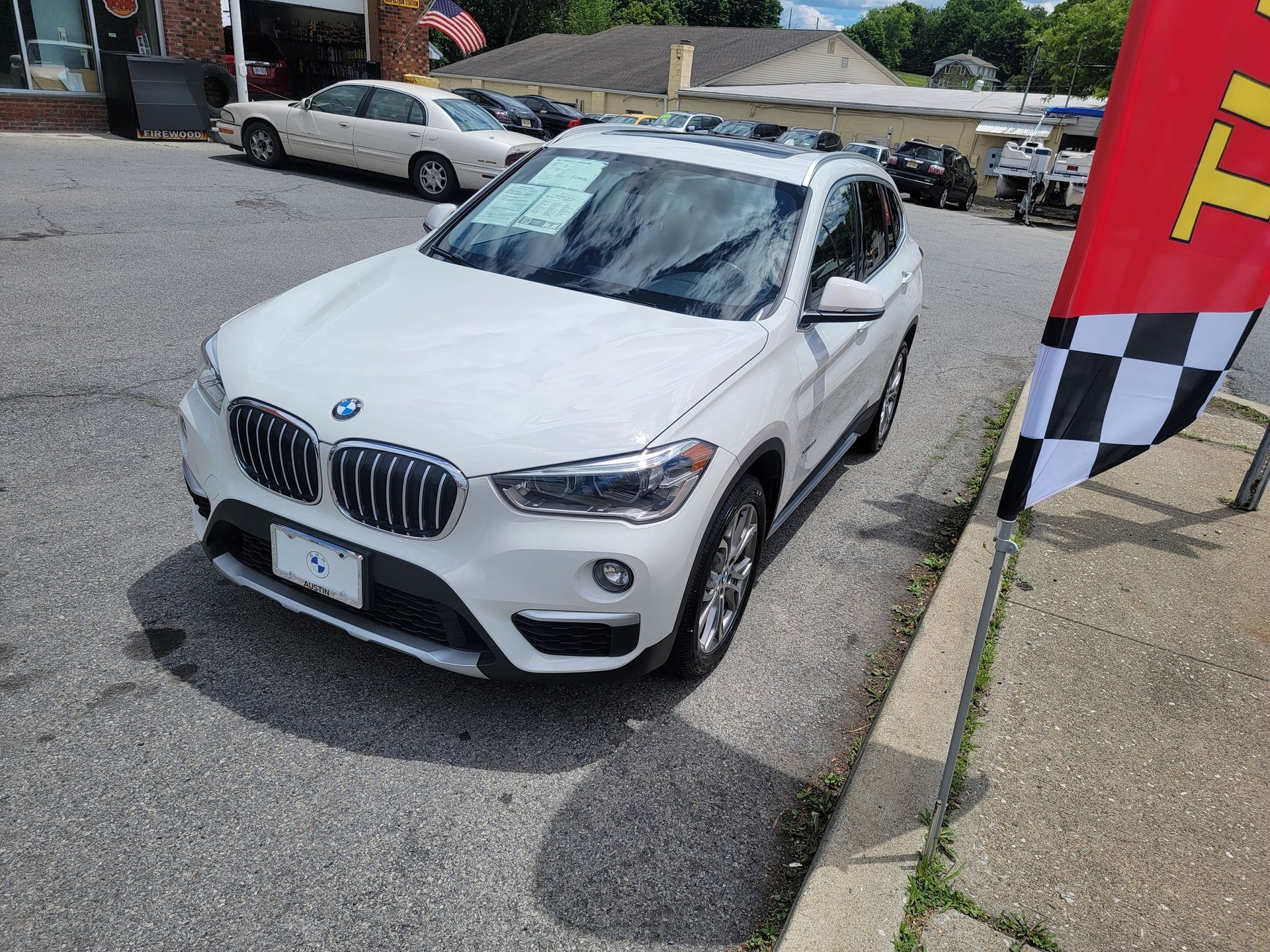 White BMW X1 SUV parked on asphalt in front of a building with a checkerboard flag.