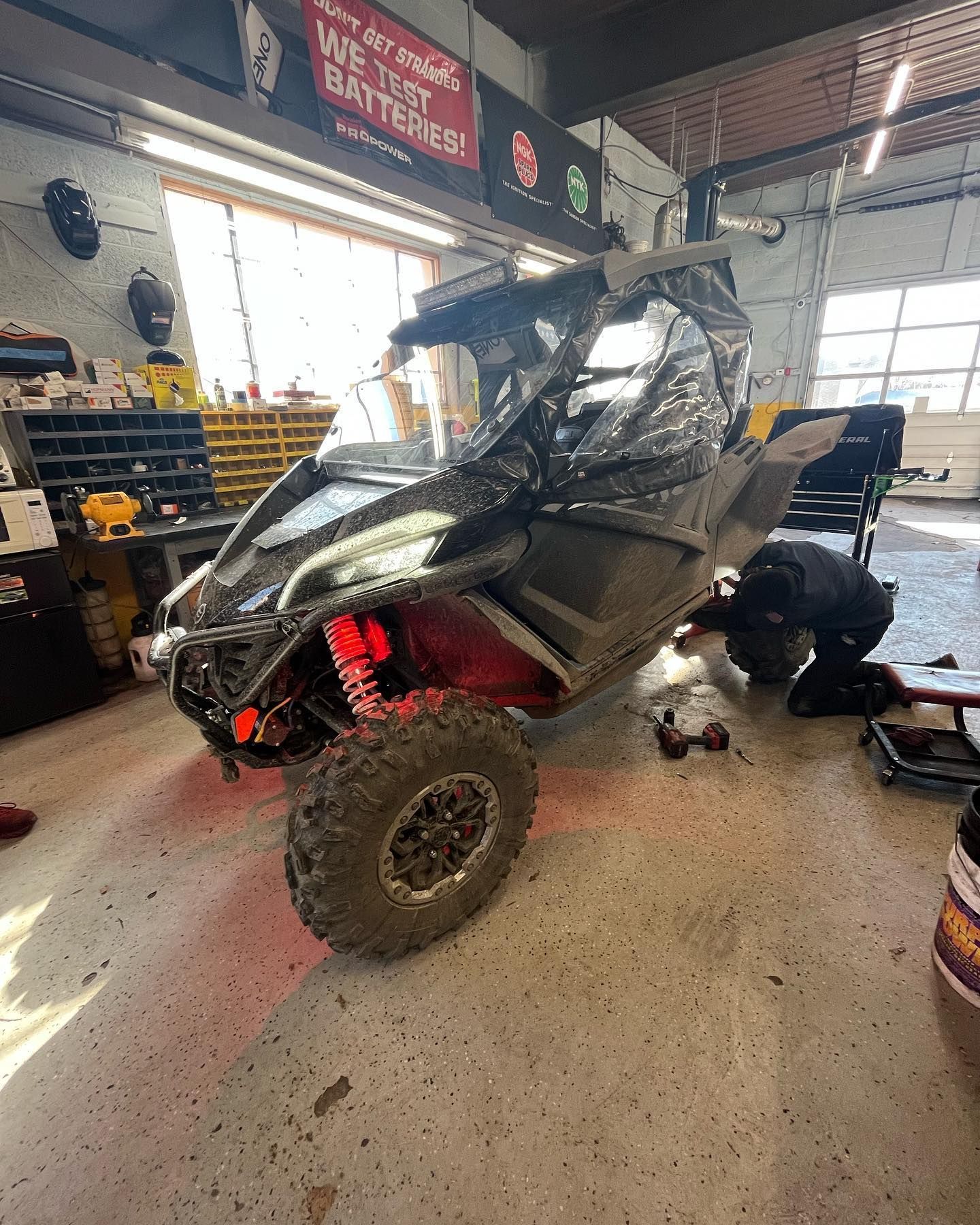 Black ATV with red accents in a garage; a person works on it.