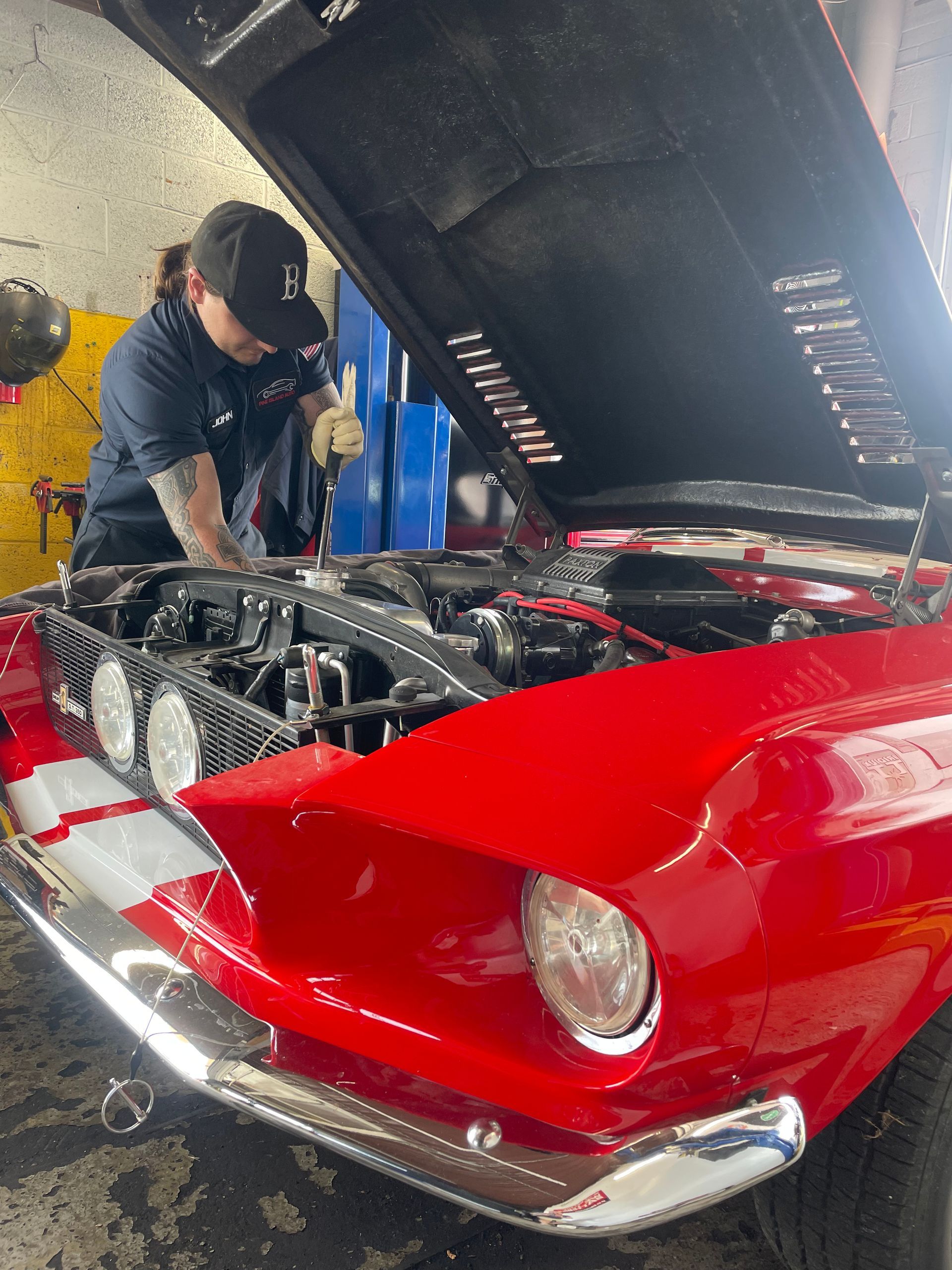 Mechanic working on a red classic car with the hood open in a garage.