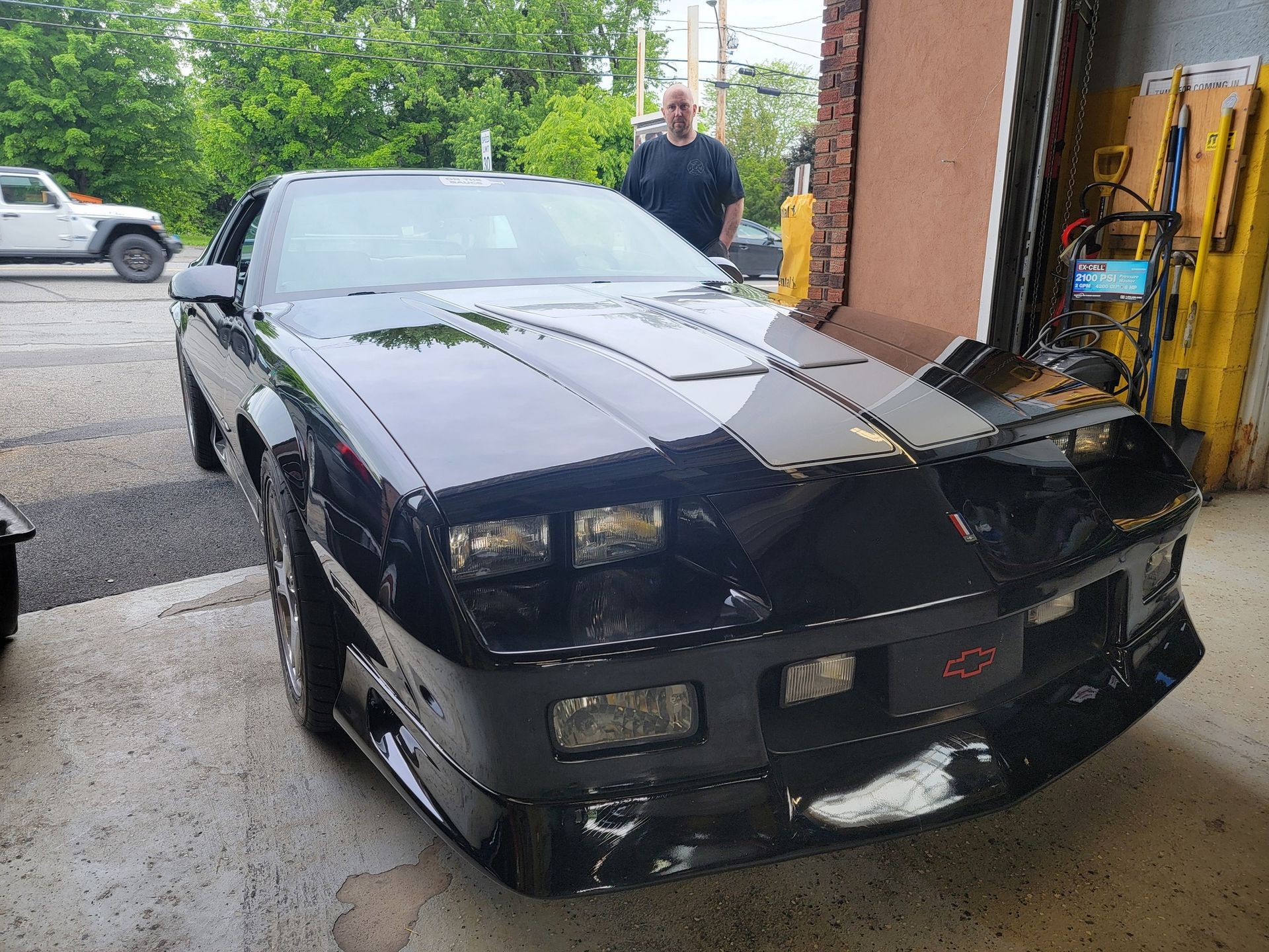 Black Chevrolet Camaro parked in a garage, with a man standing near it.