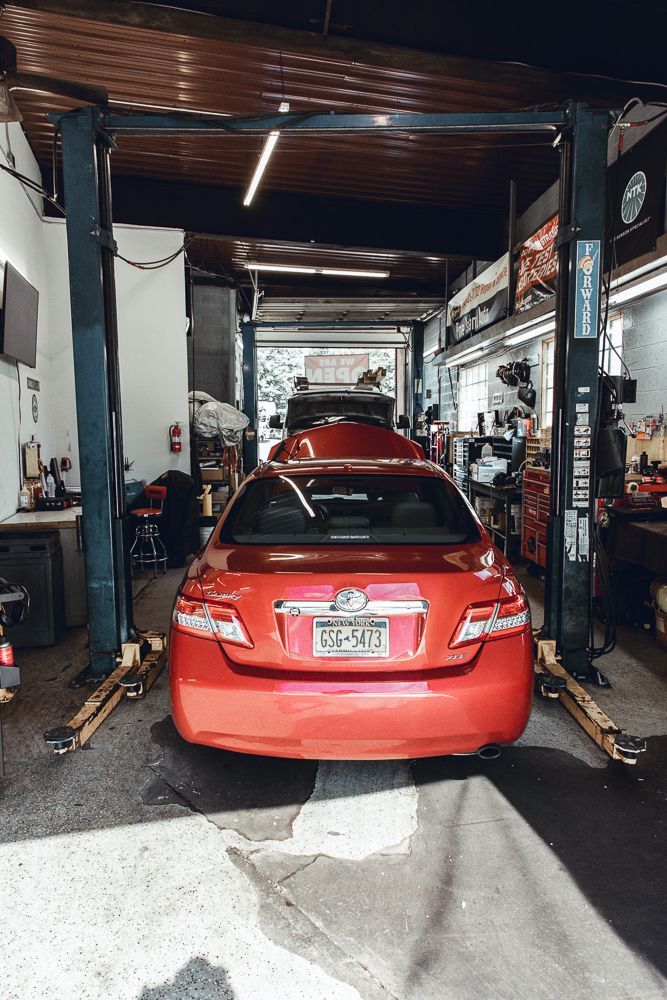 Red car inside a car repair shop, lifted on a hydraulic lift.