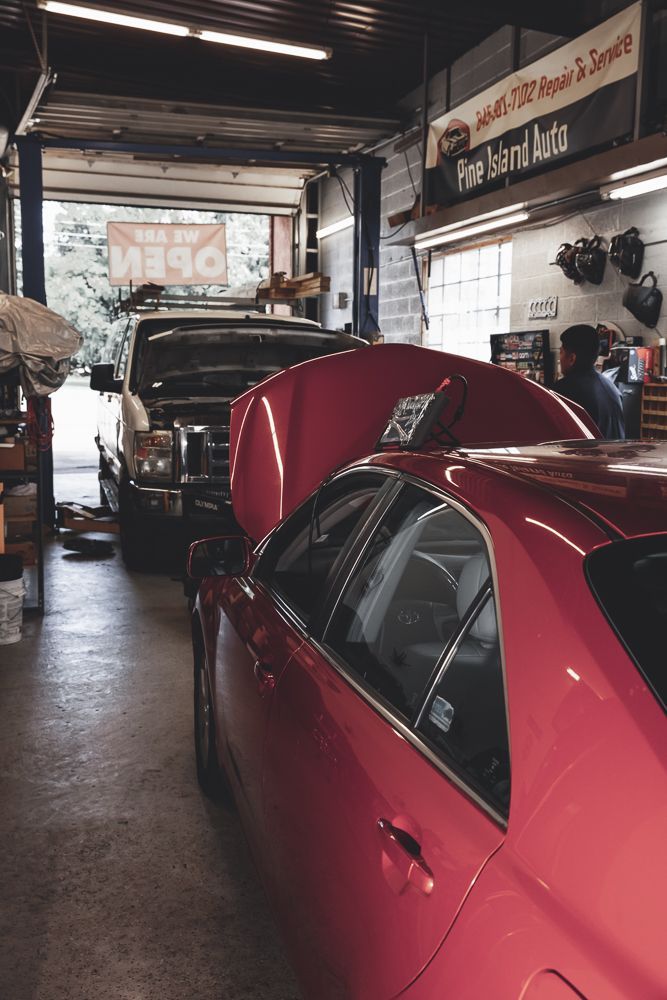 Inside auto repair shop: red car in foreground, truck in background, hood open. 