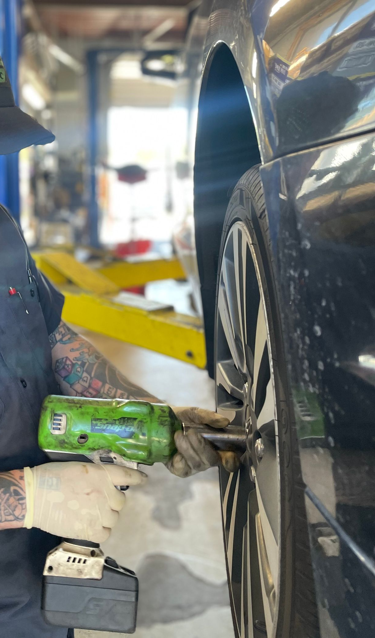 Mechanic using a power tool on a car wheel in a garage.