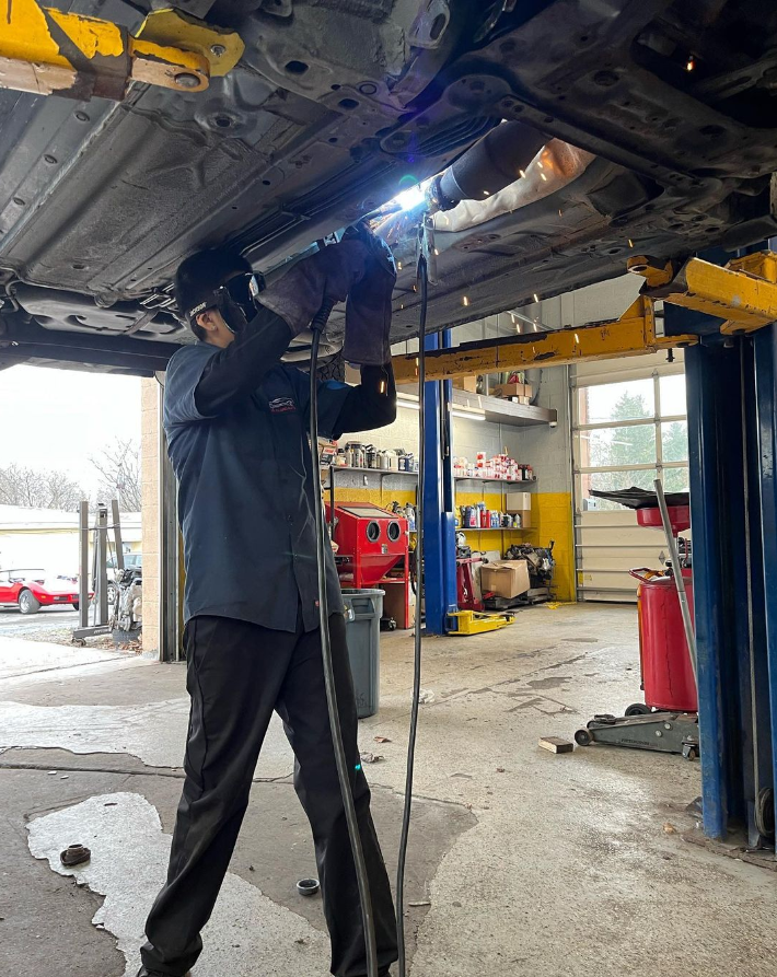 Mechanic welding under a car raised on a lift inside a shop.