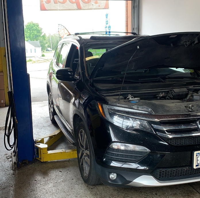 Black SUV with open hood, on a lift in a garage.