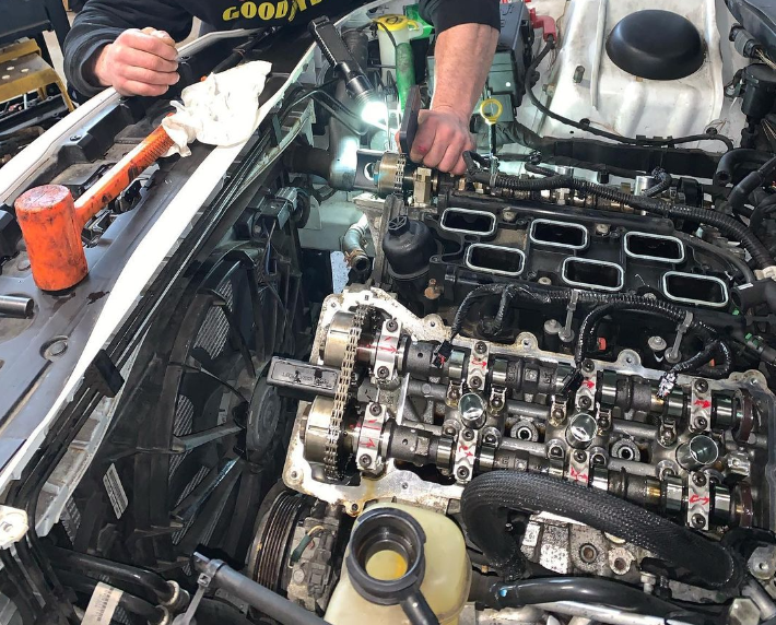 Mechanic working on a car engine, tools and parts visible. In a garage setting.