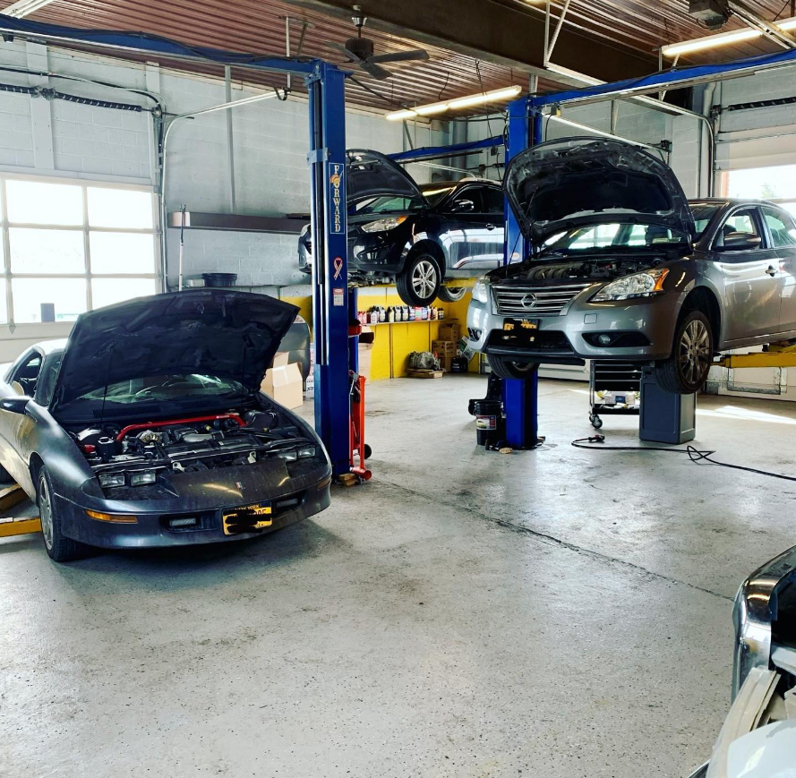 Cars on lifts inside a garage. One car has its hood up. The garage is brightly lit.