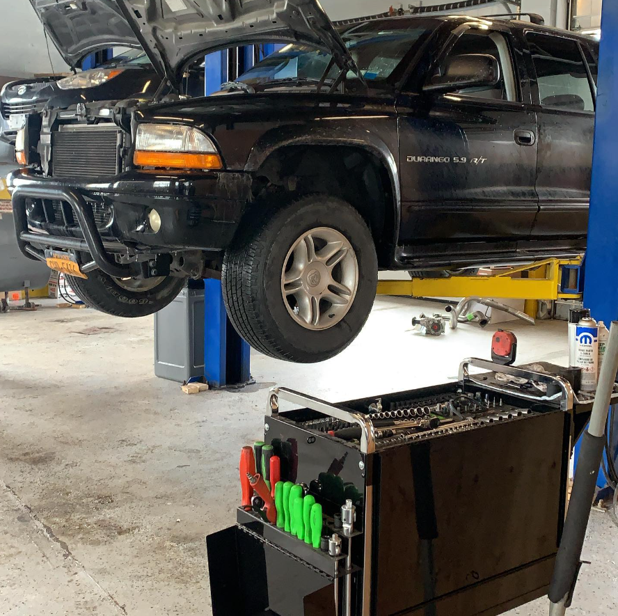 Black Dodge Durango SUV on a lift in a garage, hood open, tools in foreground.