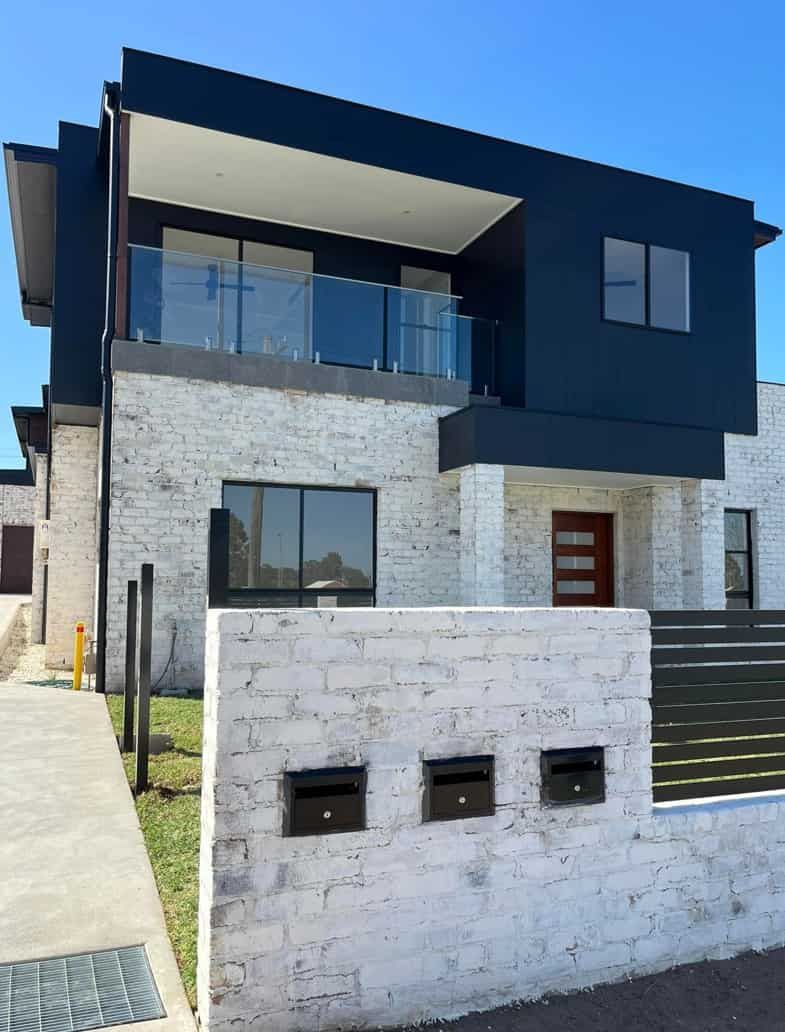 A Black And White House With A Brick Wall In Front Of It — Lamont Builders In Woonona, NSW