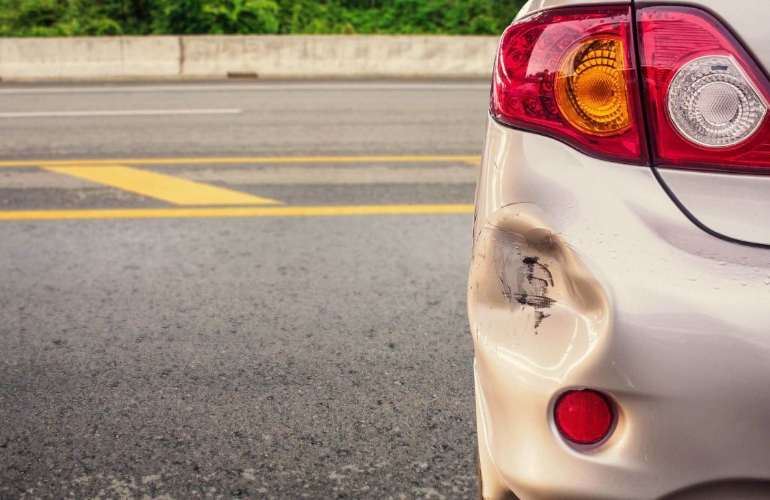 A White Car With a Damaged Bumper is Parked on the Side of the Road  — Greg Hennessey Smash Repairs In Woolgoolga, NSW