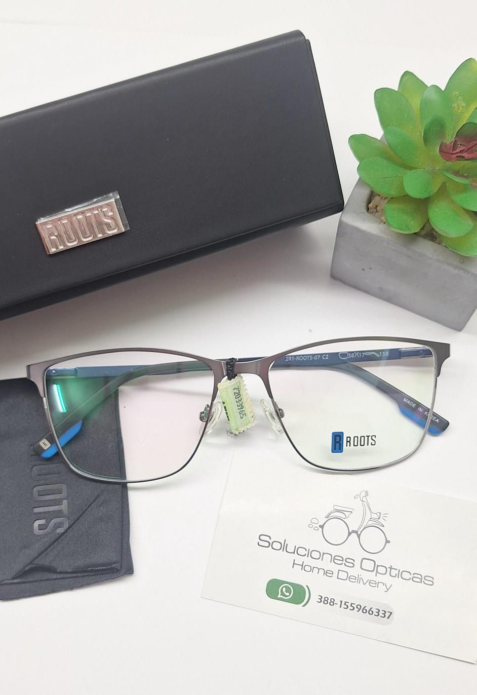 Gafas con estuche y paño de limpieza, junto a una pequeña planta y una tarjeta de visita.
