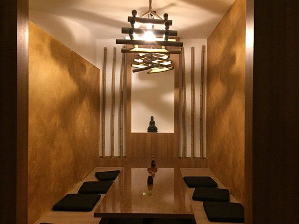 Mensa privato in toni bruni,stanghe di legno nella parete, tavola bassa di legno e i cuscini oscuri, un Buddha e luci soft lo completano