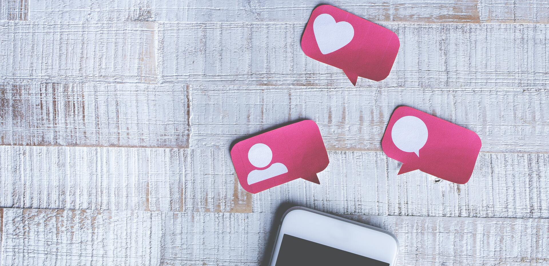 a cell phone is sitting on a wooden table next to three pink speech bubbles .