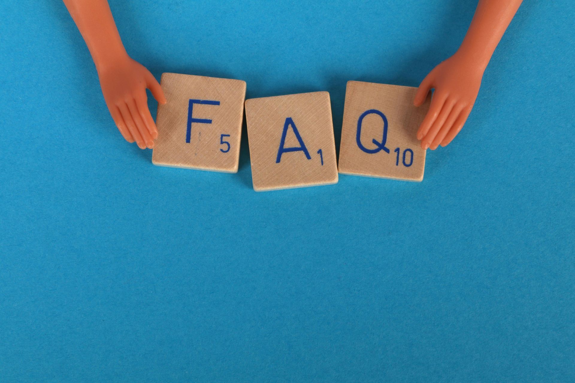 A doll 's hands are holding scrabble tiles that spell out the word faq.