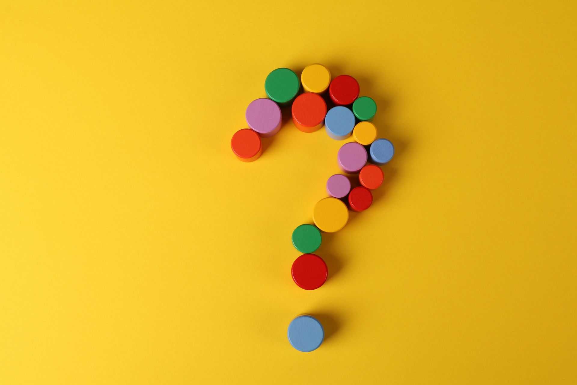 A question mark made of colorful wooden blocks on a yellow background.