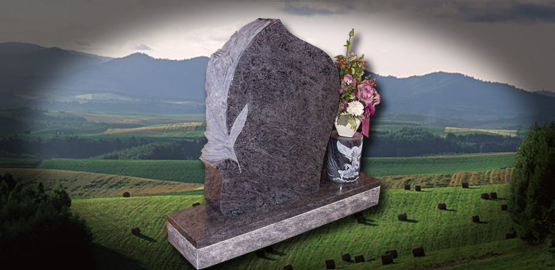 Gravestone with bird carving, flowers on a field, and mountains in the background.