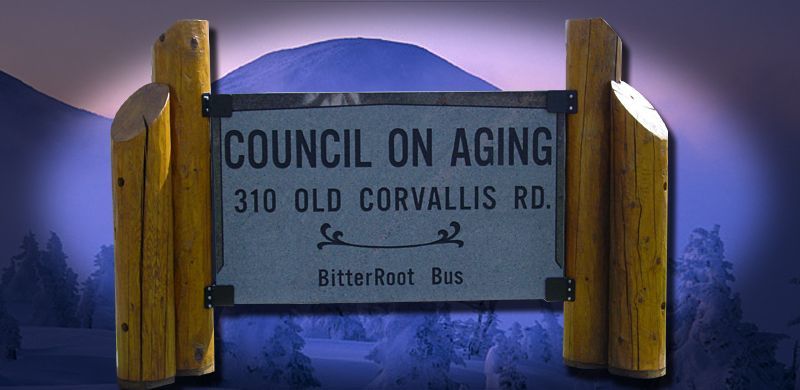 Sign for Council on Aging at 310 Old Corvallis Rd., with BitterRoot Bus information, against a mountain backdrop.