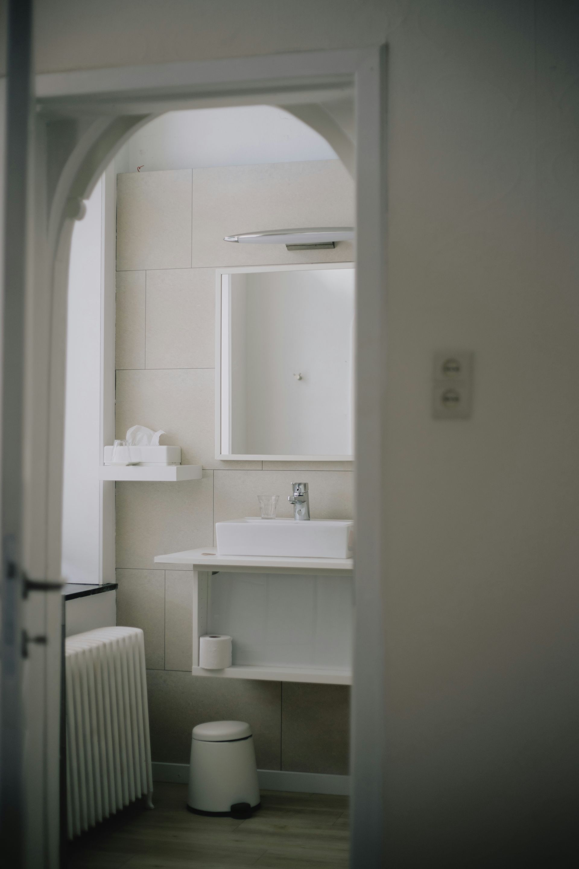 Bathroom interior with arched doorway, white sink, and radiator.