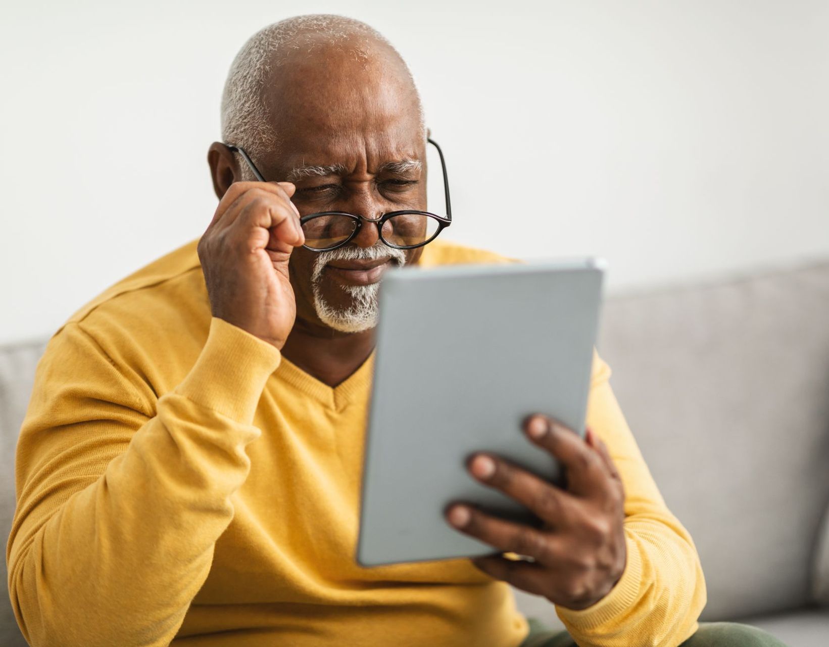 senior black man in yellow sweater struggles to read his tablet