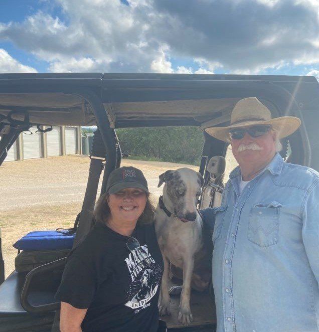A Man And Woman Are Standing Next To A Dog In The Back Of A Vehicle