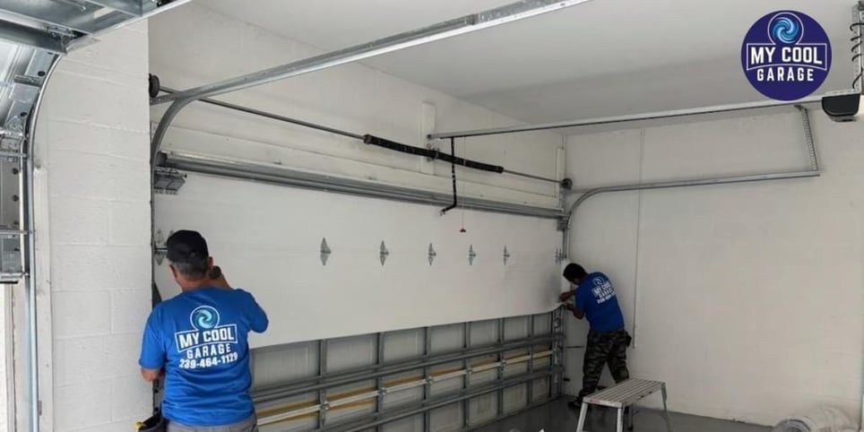 Two men in blue shirts are working on a garage door.