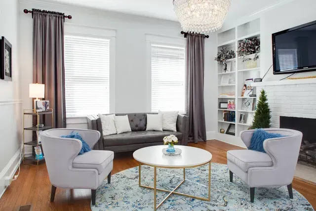 Living room with gray sofa, light blue chairs, round coffee table, chandelier, and built-in shelves.