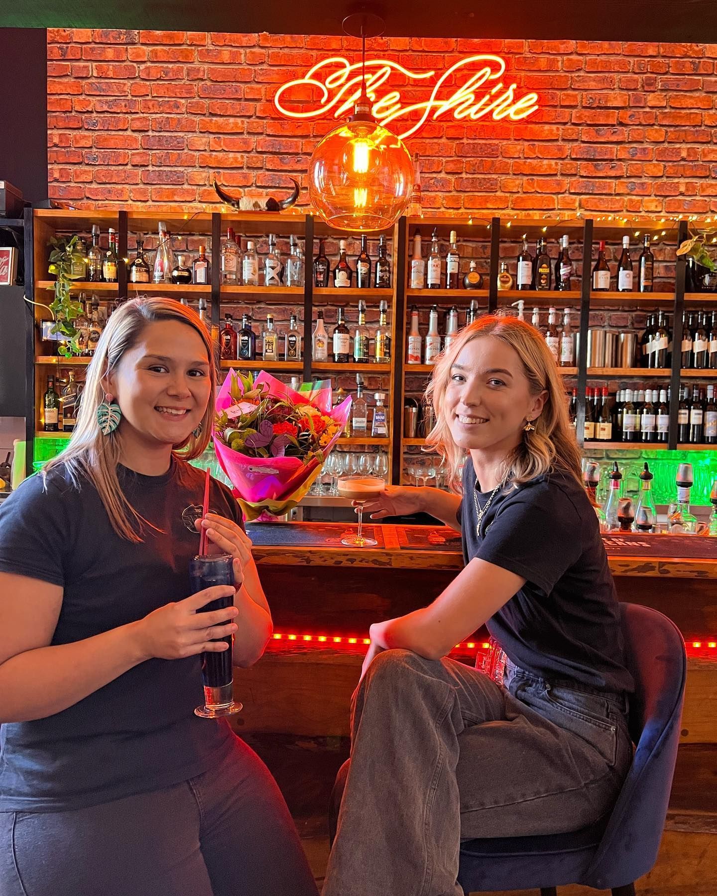 Two Women Are Sitting at a Bar Holding Drinks — The Shire Bar & Grill In Dubbo, NSW