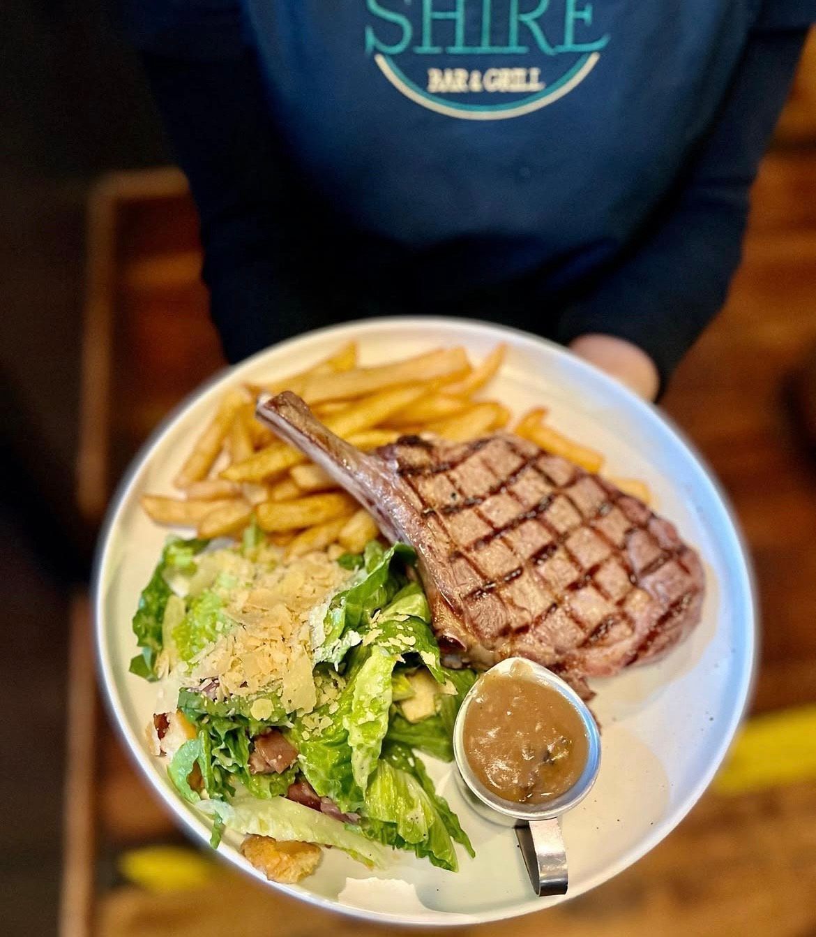A Person is Holding a Plate of Food With a Steak and French Fries — The Shire Bar & Grill In Dubbo, NSW