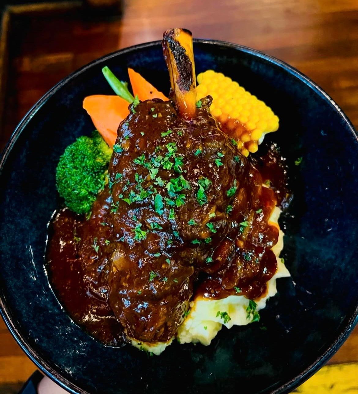 Slow-cooked lamb shank with gravy, mashed potato, and vegetables. — The Shire Bar & Grill In Dubbo, NSW