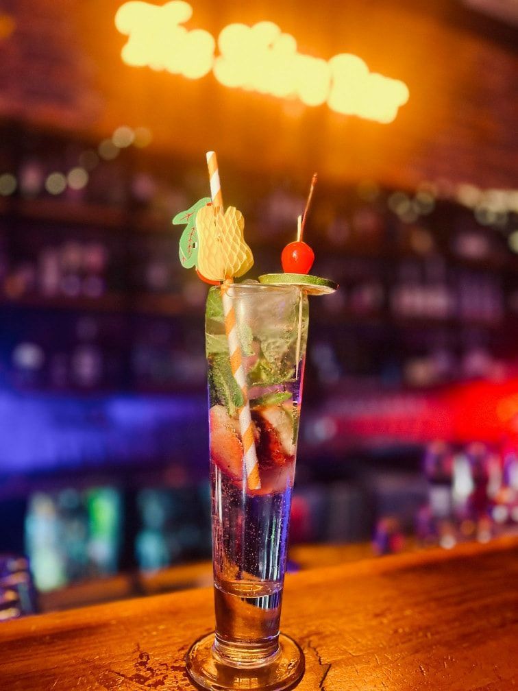 Tall Cocktail Glass With Strawberries and Mint, Garnished With a Cherry and a Straw, on a Bar — The Shire Bar & Grill In Dubbo, NSW