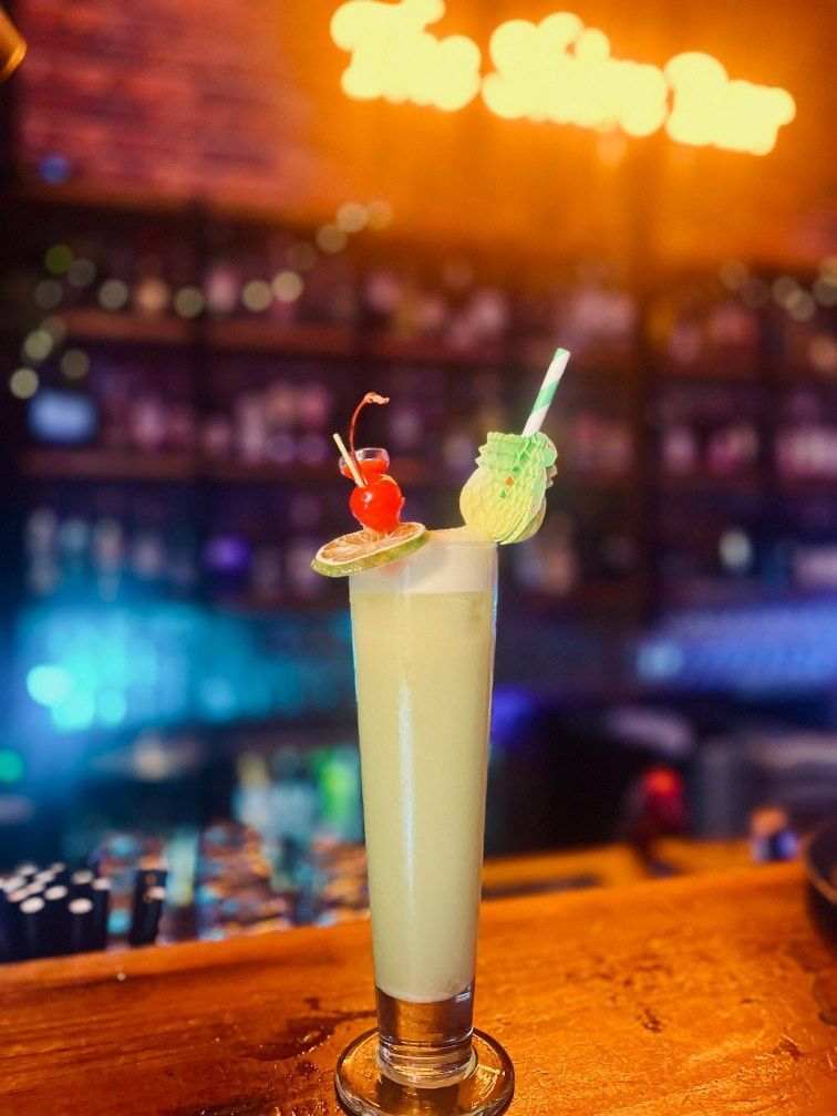 Tall Cocktail, Garnished With Cherries and Lime, Sits on Bar in Front of a Lit-up Bar Sign — The Shire Bar & Grill In Dubbo, NSW