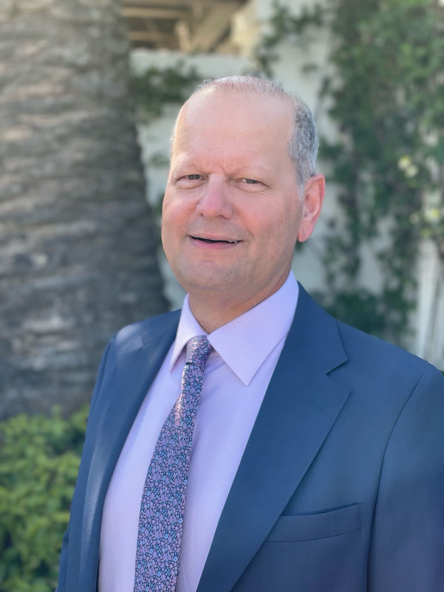 A man in a suit and tie is standing in front of a palm tree.