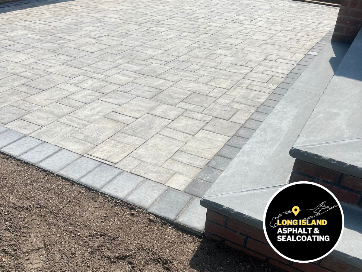 A gray brick masonry patio with bordering steps and brown grass. The Long Island paving logo is visible.
