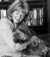 A woman is holding a dog in her lap in front of a bookshelf.