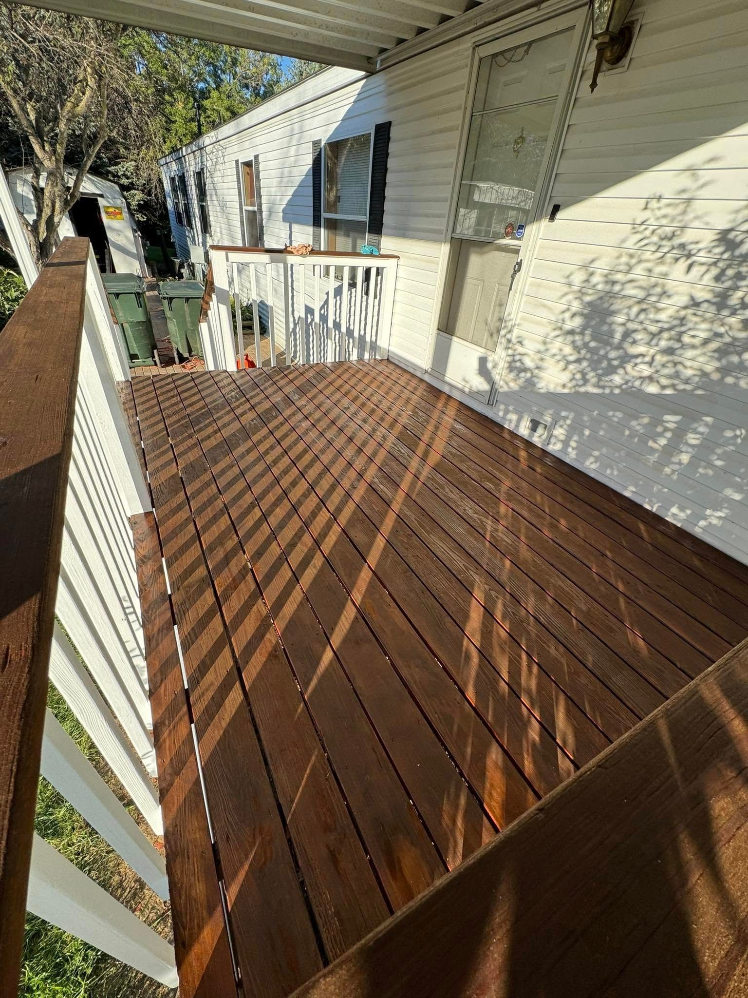 A wooden deck with stairs leading up to it and a white house in the background.