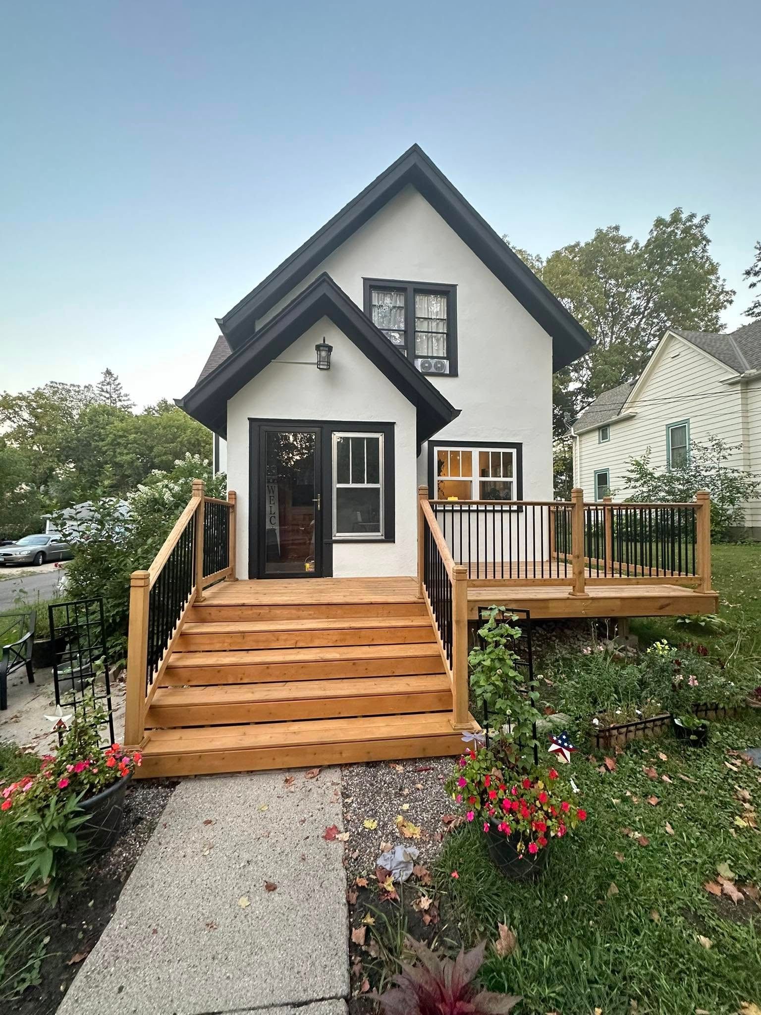 A small white house with a wooden deck and stairs leading up to it.