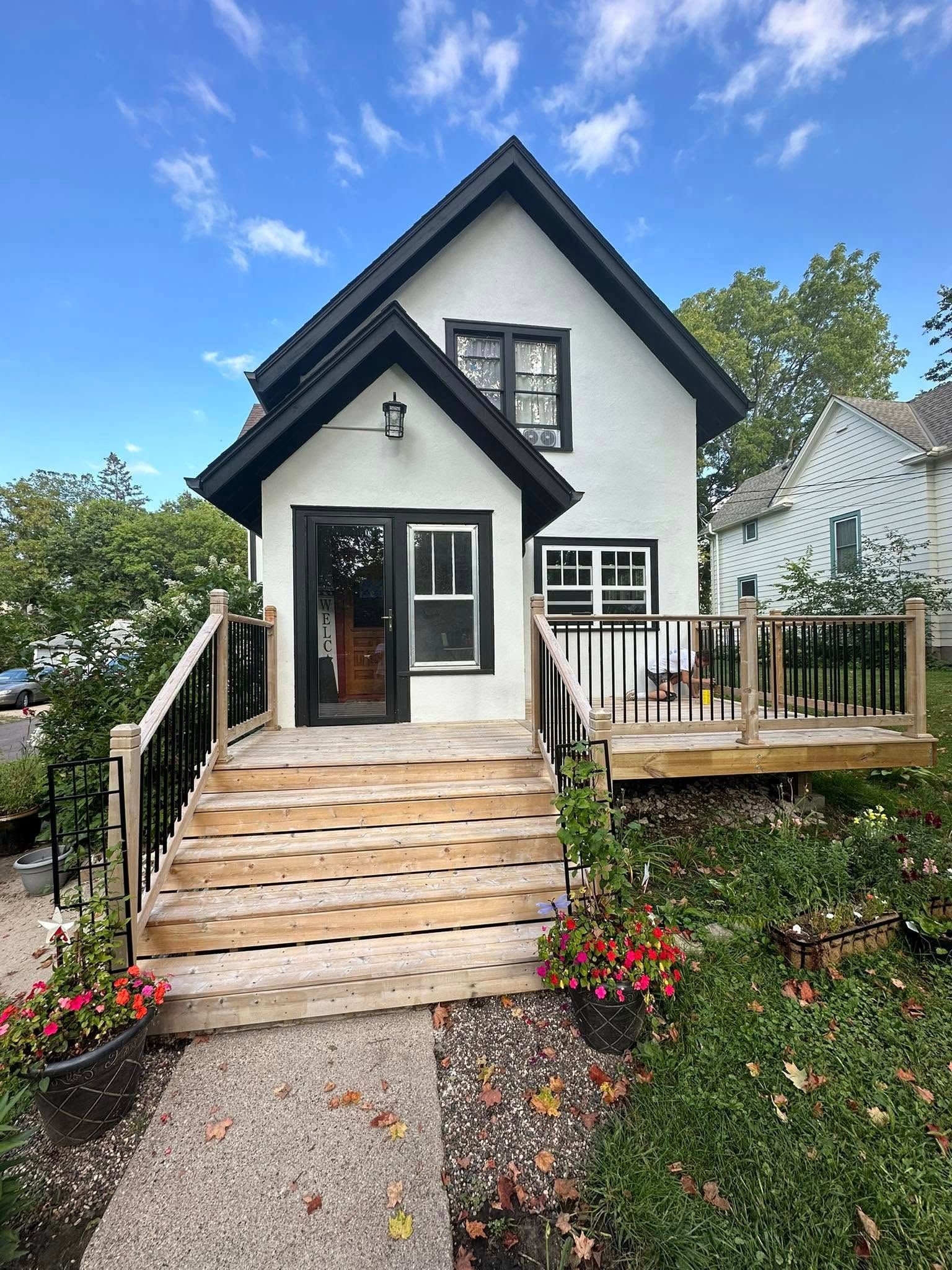 A small white house with a wooden deck and stairs leading up to it.