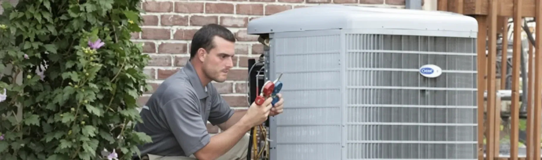 HVAC technician working on an air conditioner unit, outdoors near a brick wall and wooden fence.