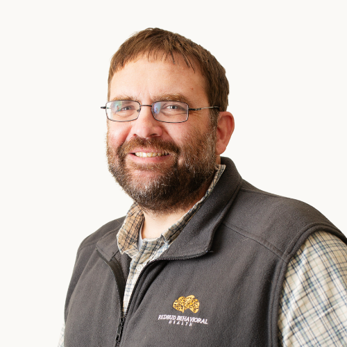Man in glasses and vest smiles. Florida Memorial University logo on vest.