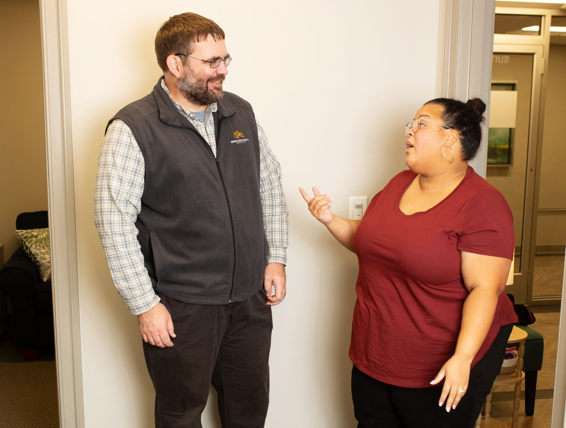 A man and woman talking in a doorway. The woman gestures with her hand as the man smiles.