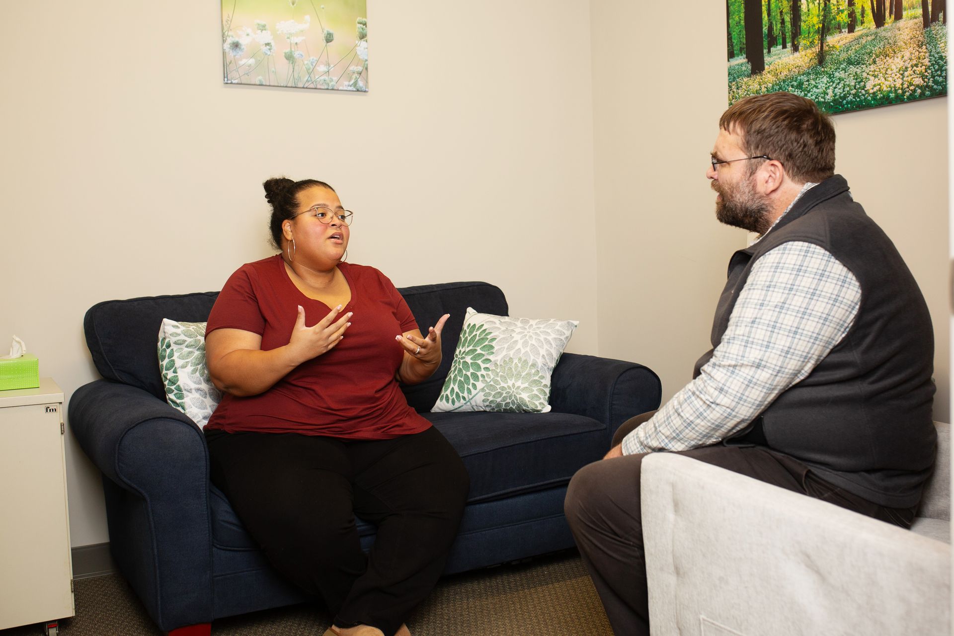 Woman on a couch gesturing as she talks to a man seated opposite her in a counseling session.
